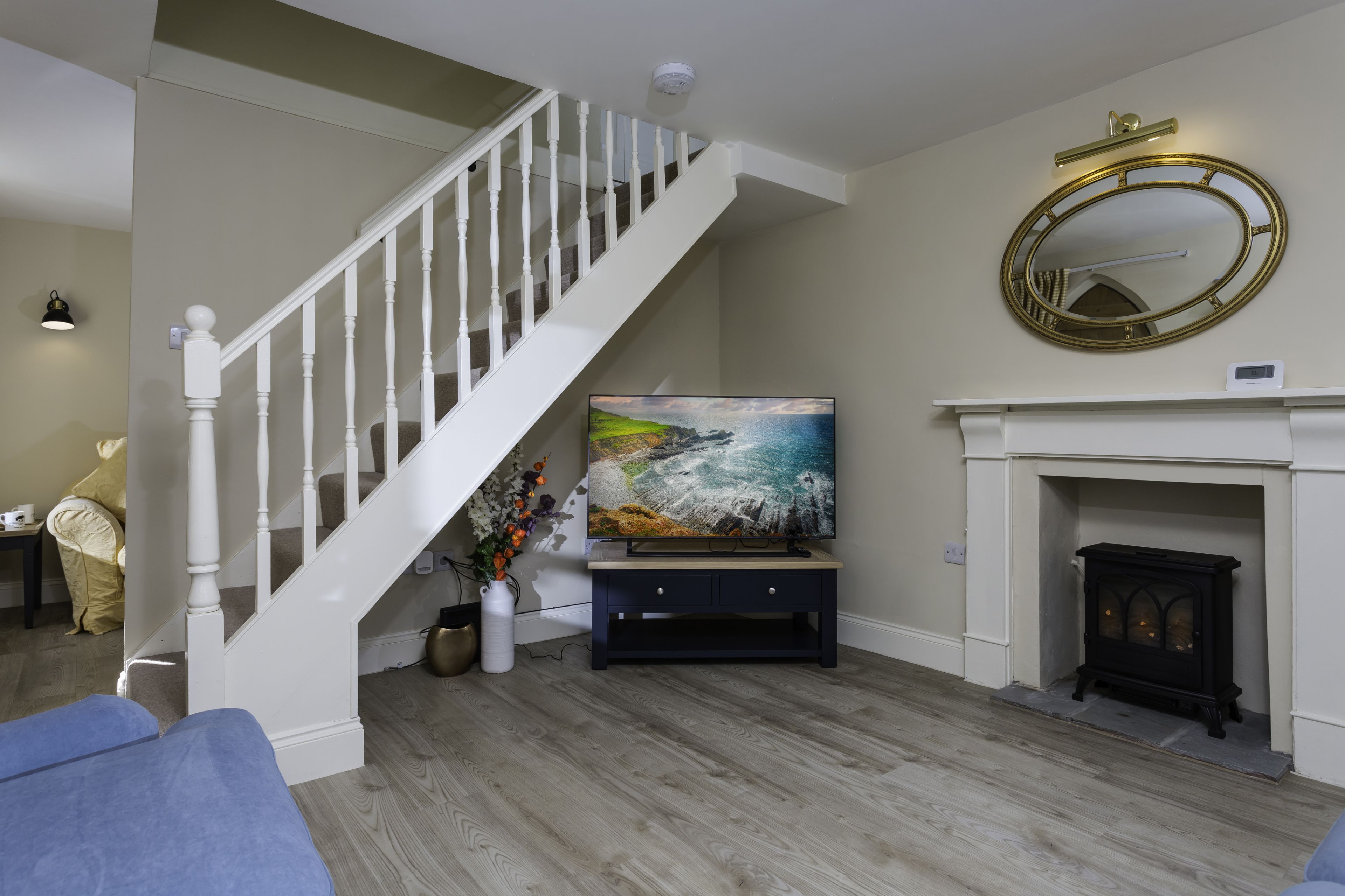Living room showing white staircase and coastal scene on TV