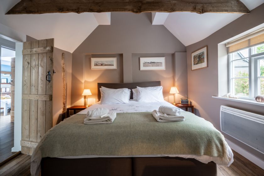 Bedroom with wooden beams, grey walls, white linens and rustic wooden door