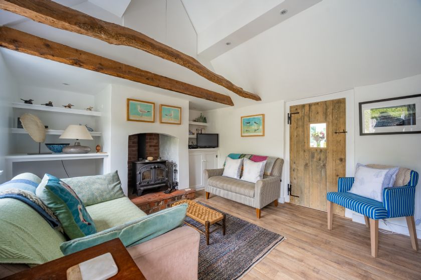 Living room with exposed wooden beams, wood stove and pastel furniture