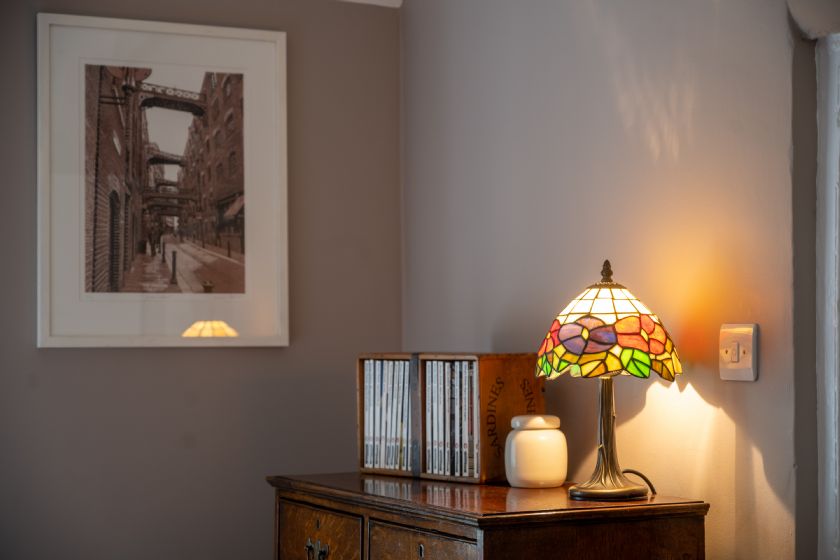 Sideboard with Tiffany-style lamp, CDs and framed artwork on grey wall