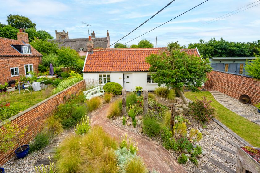 Aerial view of white cottage with terracotta roof and garden with ornamental grasses