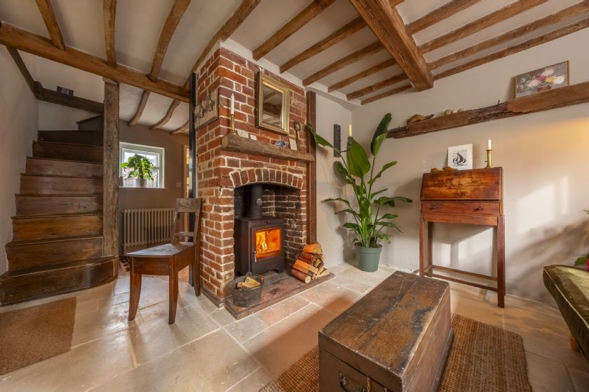 Living room with wooden beams, brick fireplace with wood stove and wooden staircase