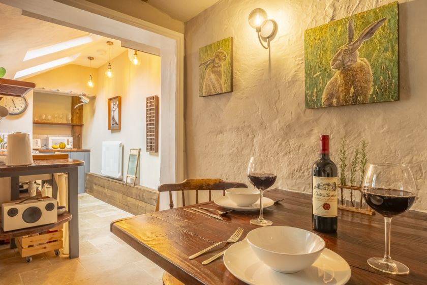 Dining area with wooden table, wine glasses and hare artwork on textured white walls