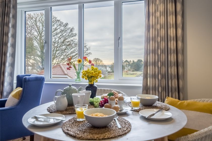 Breakfast table with food, flowers, and a view from windows