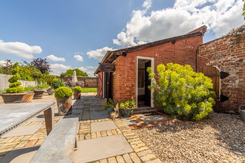 Brick outbuilding with yellow bushes and stone patio