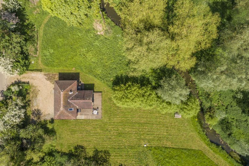 Aerial view of cottage surrounded by countryside and stream